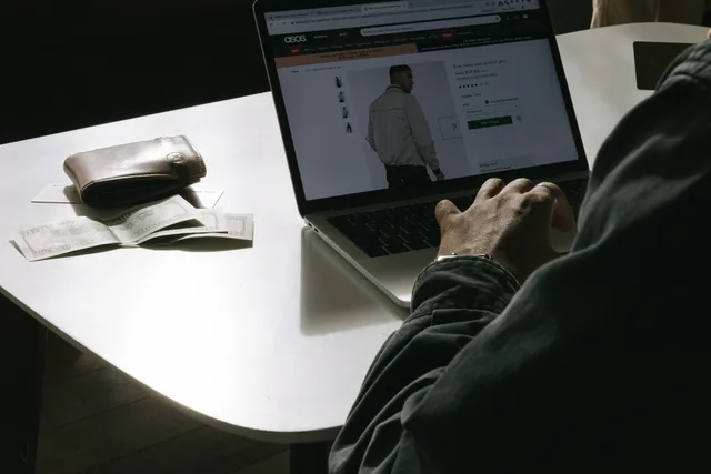 Adult man shopping for clothes online at home using a laptop, with a wallet on the table. Sprzedaż omnichannel: łączenie sklepu, e-commerce i danych